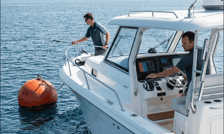 Duracordix - Your Trusted Supplier for High-Performance Synthetic Rope & Netting | How To Do Mooring Buoy Setup? A Complete Guide! A professional crew on a luxury motor yacht demonstrating a precision mooring maneuver. One crew member at the bow uses a boat hook to secure a DURACORDIX high-performance mooring line to a large orange surface buoy, while the captain coordinates from the helm station