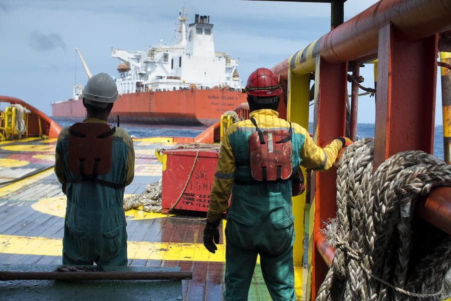 Une équipe offshore supervise une opération d'amarrage et de remorquage lourd d'un FPSO depuis le pont d'un bateau de travail, un grand navire étant positionné en mer ouverte.